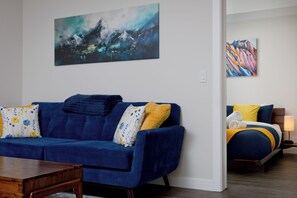 Een moderne woonkamer met een blauwe bank, een houten salontafel en een schilderij van een berglandschap.