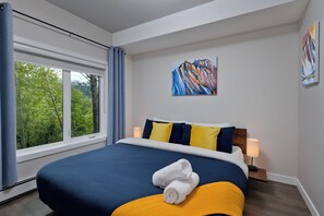 Een hotelkamer met een groot bed, een raam met gordijnen, een schilderij aan de muur en een nachtkastje met een lamp.