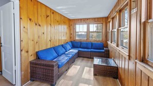 Ein Zimmer mit einer großen Wand aus Holzpaneelen, einem blauen modularen Sofa, einem Glastisch und einer Tür.