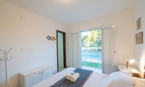 A hotel room with a bed, a desk with a lamp, a coat rack, and a sliding door to a balcony. - House w/ Pool 200 m From the Beach Pro0003 (Camaçari)