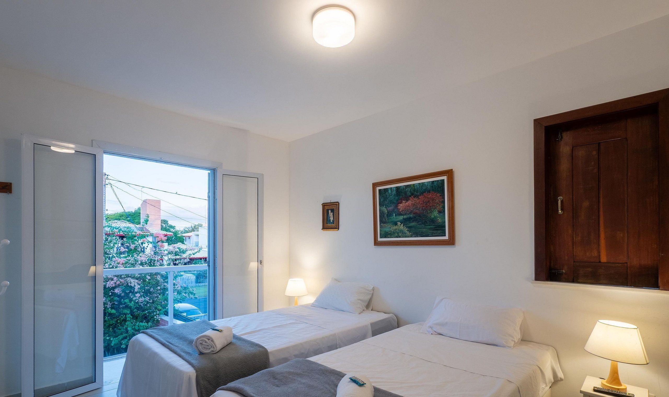 Habitación de hotel con dos camas, una ventana con vistas a la vegetación, un cuadro en la pared y una puerta de madera.