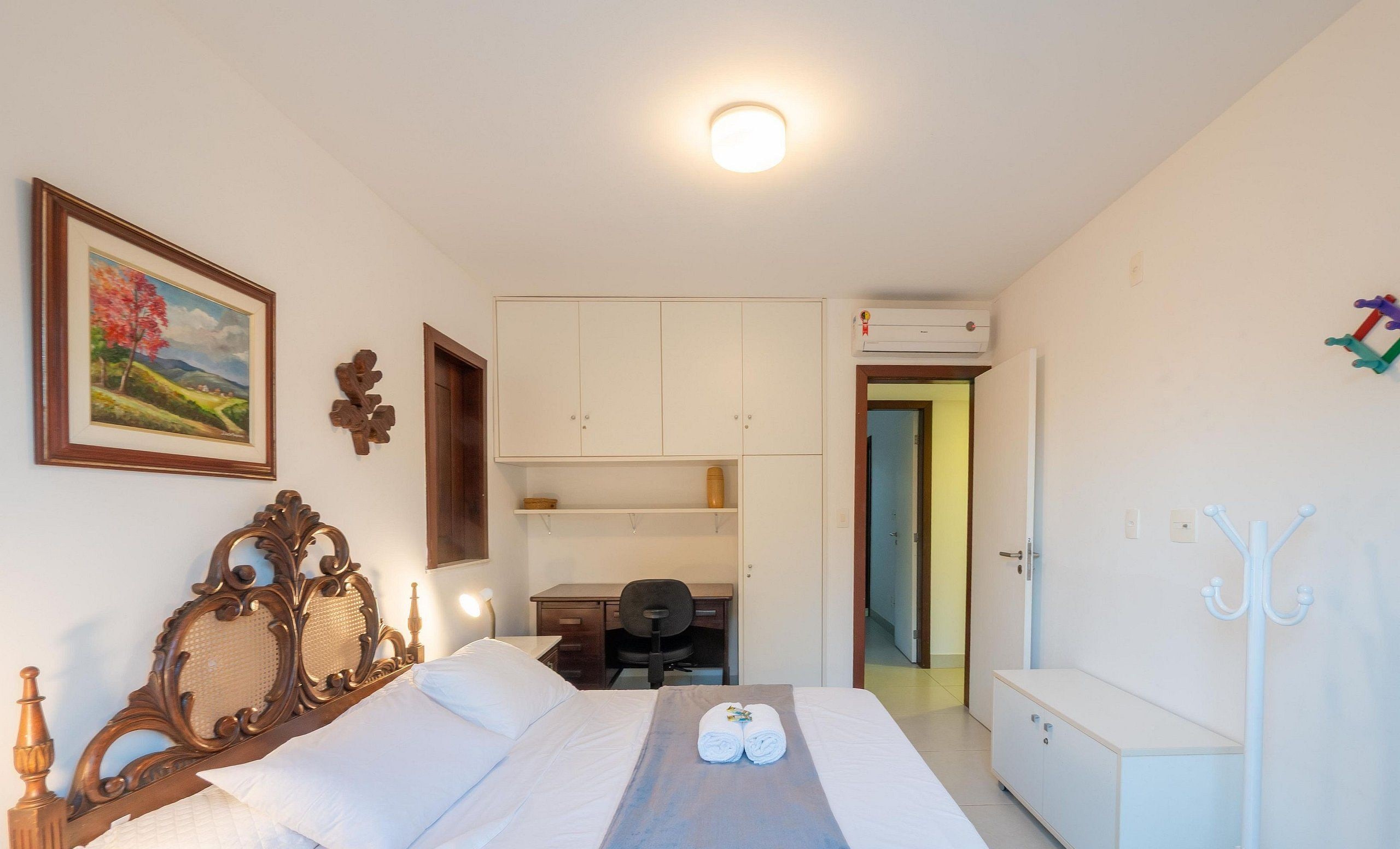 Quarto de hotel com cama, escrivaninha, cadeira, guarda-roupa e cabideiro.