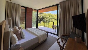 A modern hotel room with a large bed, a desk, a TV, and a balcony with a view of greenery. - Lujo Frente al Mar para 8 (Nay.)