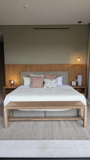 Ein modernes Schlafzimmer mit einem Holzkopfteil, einem großen Bett mit vielen Kissen, Nachttischen mit Lampen und einer hängenden Leuchte.