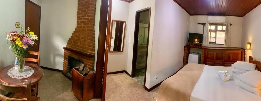 A hotel room with a bed, a small table with a vase of flowers, a brick fireplace, and a television on a wooden cabinet.