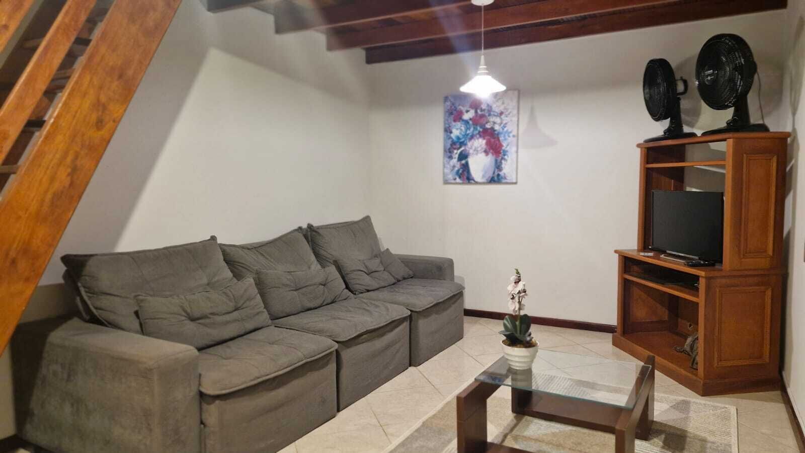 A living room with a grey sofa, a glass coffee table, a TV on a wooden stand, and a painting on the wall.