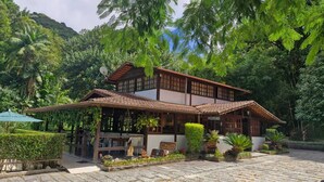 A traditional wooden building with a tiled roof, surrounded by lush greenery and a stone-paved courtyard. - Pousada Caminho das Candeias (Nova Friburgo)