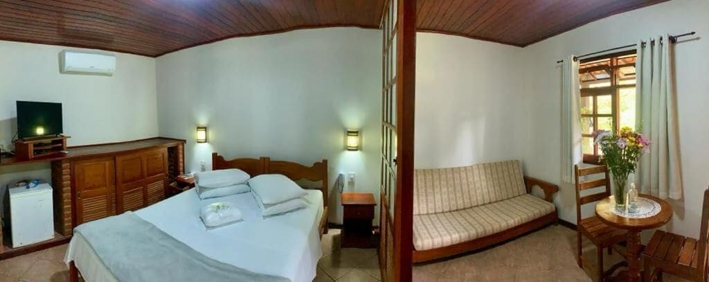 A hotel room with a bed, a sofa, a small table with a vase, and a television on a cabinet.