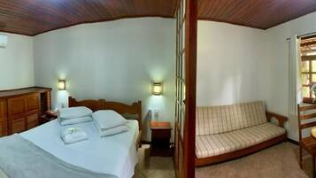 A hotel room with a bed, a sofa, a small table with a vase, and a television on a cabinet.