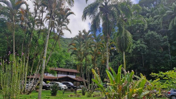 A tropical resort with a traditional building, lush greenery, and parked cars. - Pousada Caminho das Candeias (Nova Friburgo)