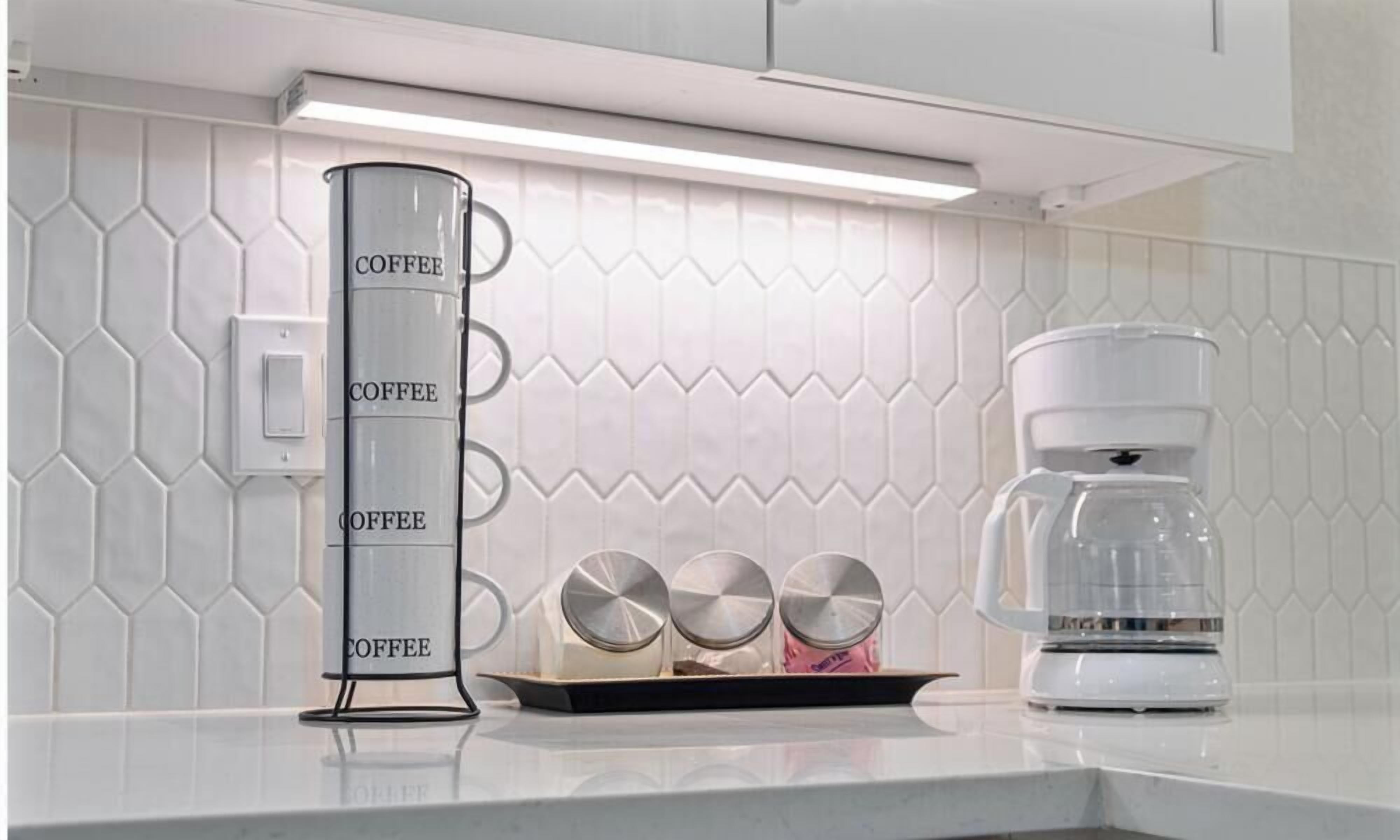 A kitchen counter with a coffee maker, a tall glass container labeled "COFFEE," and three metal coffee filters.