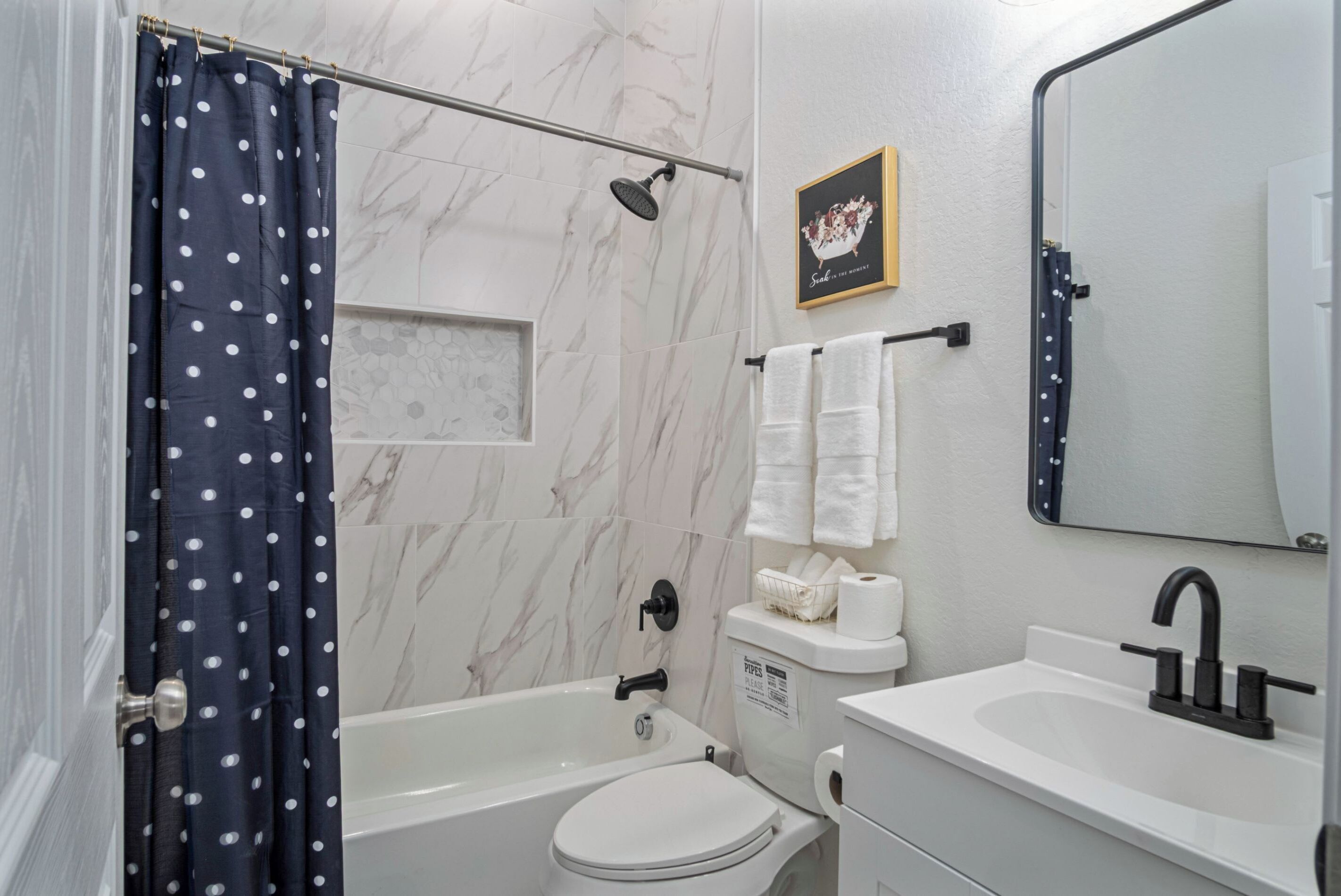 Un bagno con vasca, water, e lavabo, con pareti in marmo e una tenda per la doccia.
