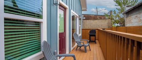 A wooden deck with two Adirondack chairs, a red door, and a brick wall.