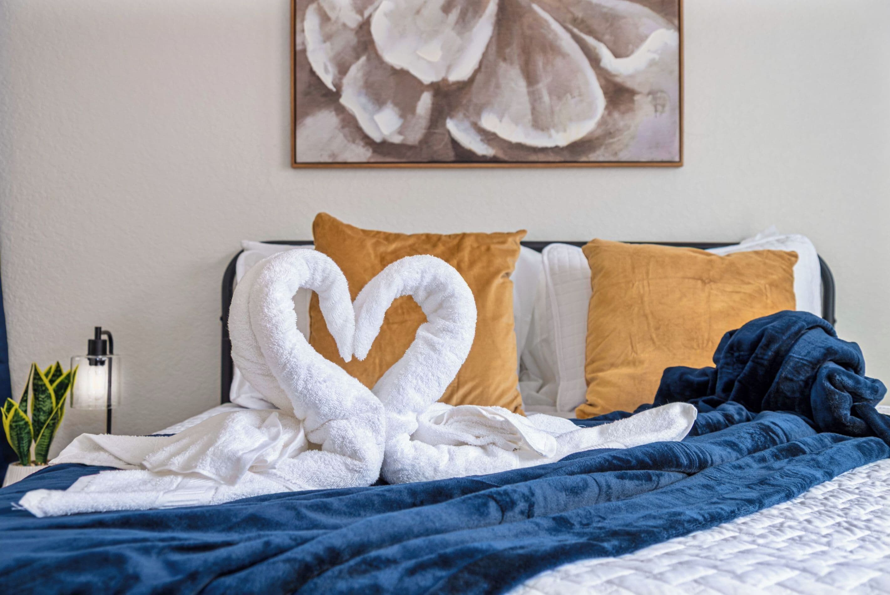 A neatly made bed with a blue blanket and two pillows, one brown and one white.
