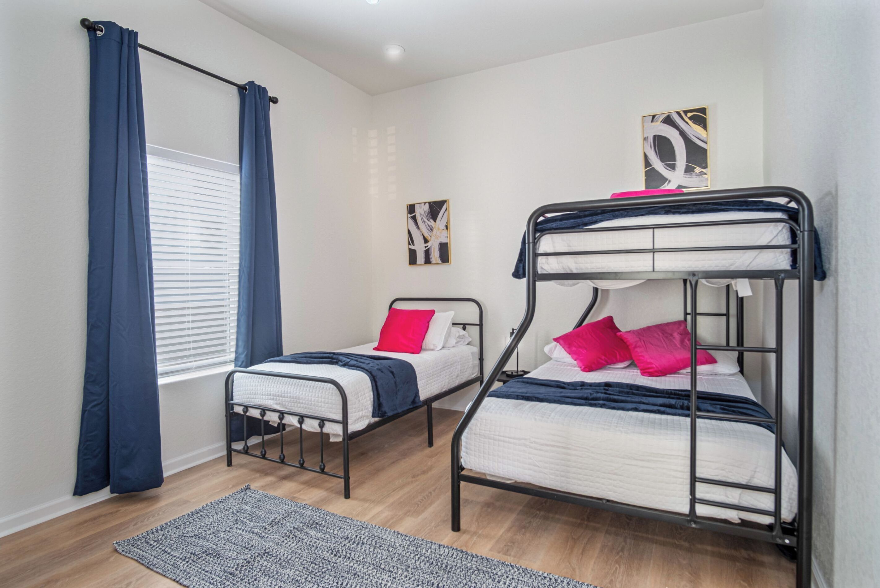 Una habitación con dos literas, una ventana con cortinas, una alfombra y dos cuadros en la pared.