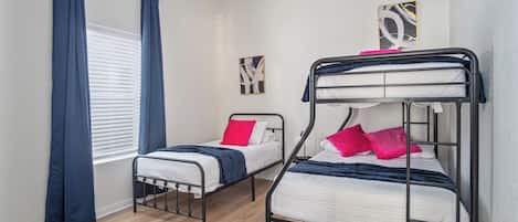A room with two bunk beds, a window with curtains, a rug, and two wall art pieces.