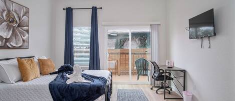 A bedroom with a bed, a desk, a chair, a TV, and a balcony with a view.