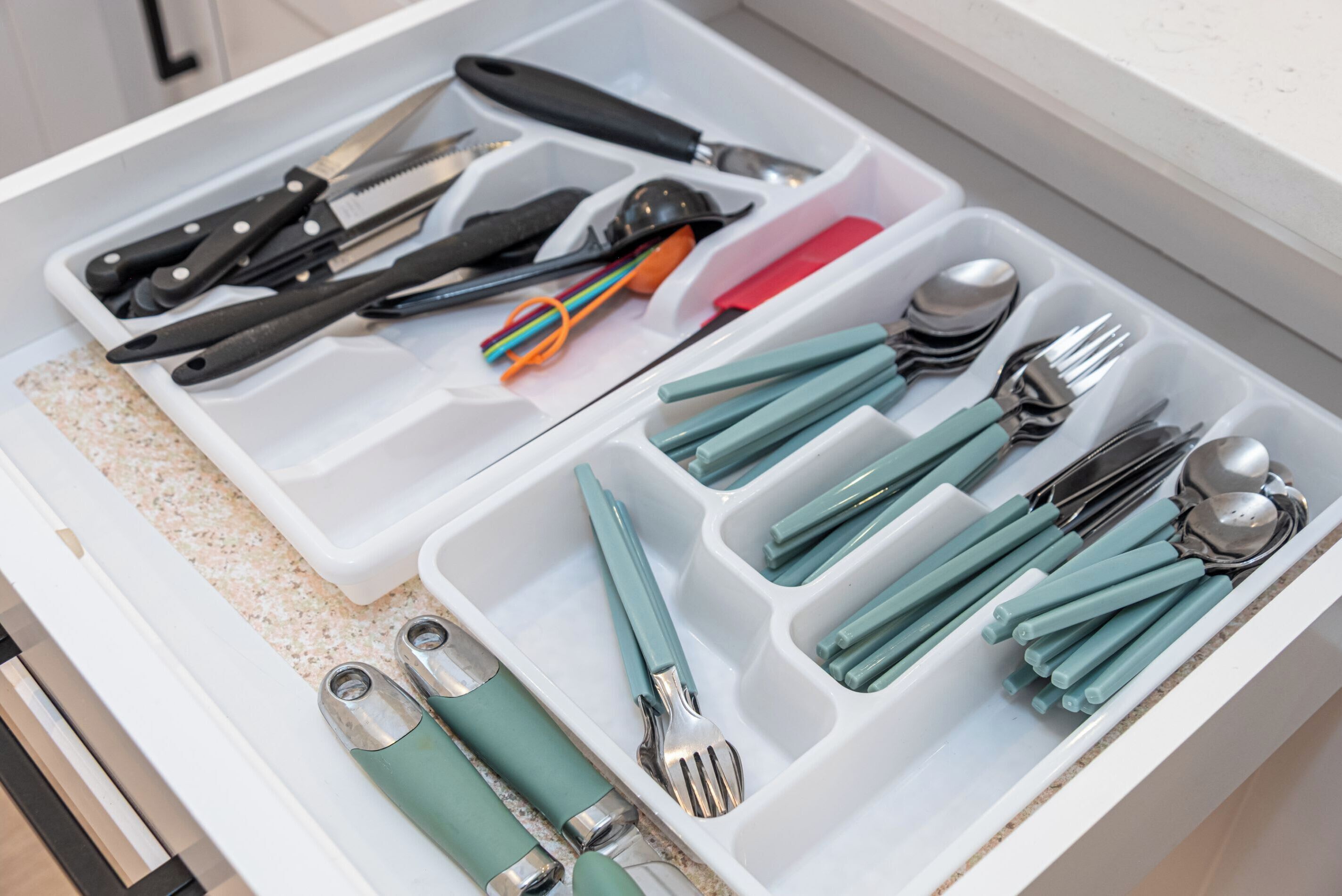 A drawer with compartments containing various kitchen utensils, including knives, spoons, and forks.