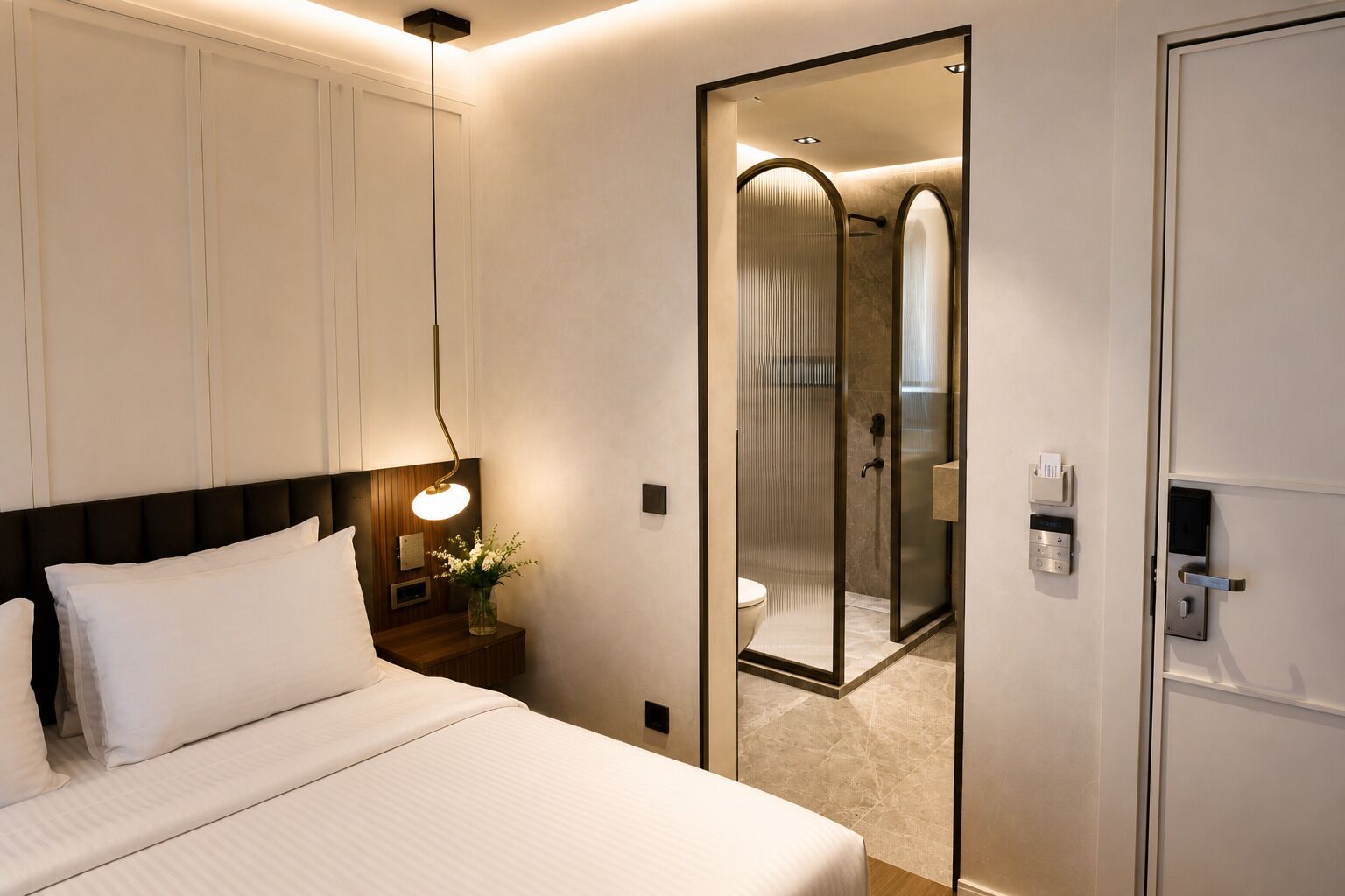 A hotel room with a bed, bedside lamp, nightstand, and a mirror reflecting a shower area.