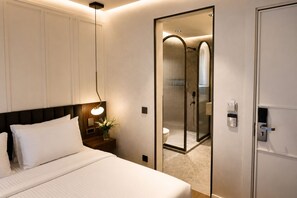 A hotel room with a bed, bedside lamp, nightstand, and a mirror reflecting a shower area. - alaturka mansion (İstanbul)