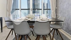 Ruokailutila, jossa on neljälle katettu pöytä, suuret ikkunat ja näkymä korkeisiin kerrostaloihin.