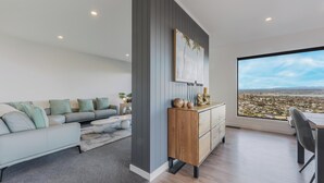 Un salón moderno con un sofá gris, un mueble de madera y un amplio ventanal con vistas a la ciudad.