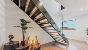 Un interior moderno con una escalera curva, un ventanal con vistas y jarrones decorativos sobre una plataforma de madera.