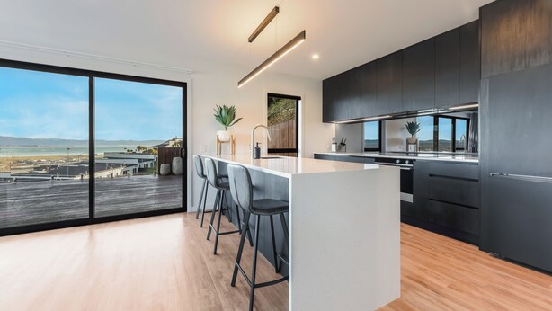 Una cocina moderna con una isla grande, taburetes de bar y vista al océano.
