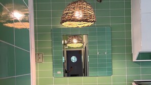 Une cuisine avec des carreaux verts, une table en bois, deux tabourets et un luminaire suspendu.
