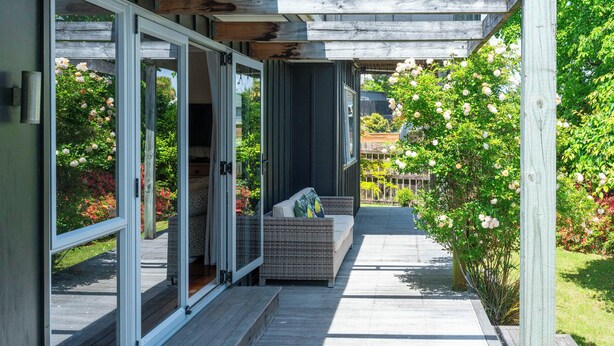 Une terrasse extérieure avec un canapé en osier et des portes-fenêtres coulissantes donnant sur un jardin.