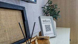 Un letrero de bienvenida enmarco con un código QR, una planta en maceta y un tapete tejido rústico.