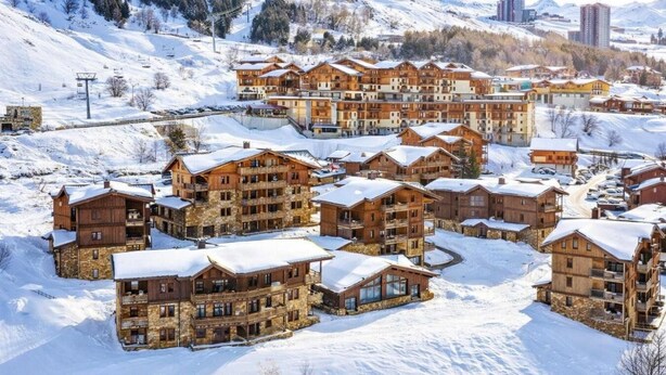 Een met sneeuw bedekt wintersportresort met meerdere houten gebouwen, skiliften en een bergachtige achtergrond.