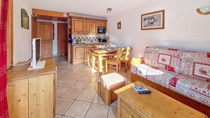 Una sala de estar acogedora con un sofá de madera, una mesa de comedor y una zona de cocina con armarios de madera y piso de baldosas.