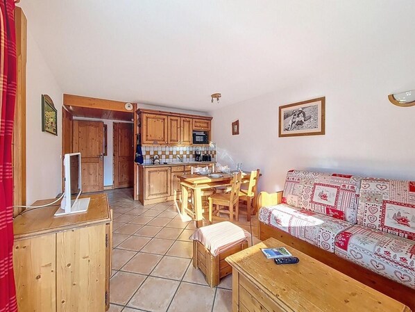 A cozy living room with a wooden sofa, a dining table, and a kitchen area with wooden cabinets and a tiled floor. - 100m from ski slopes, 1st floor, swimming pool, balcony, tv, ski locker, 50m², Les Menuires (Les Menuires)
