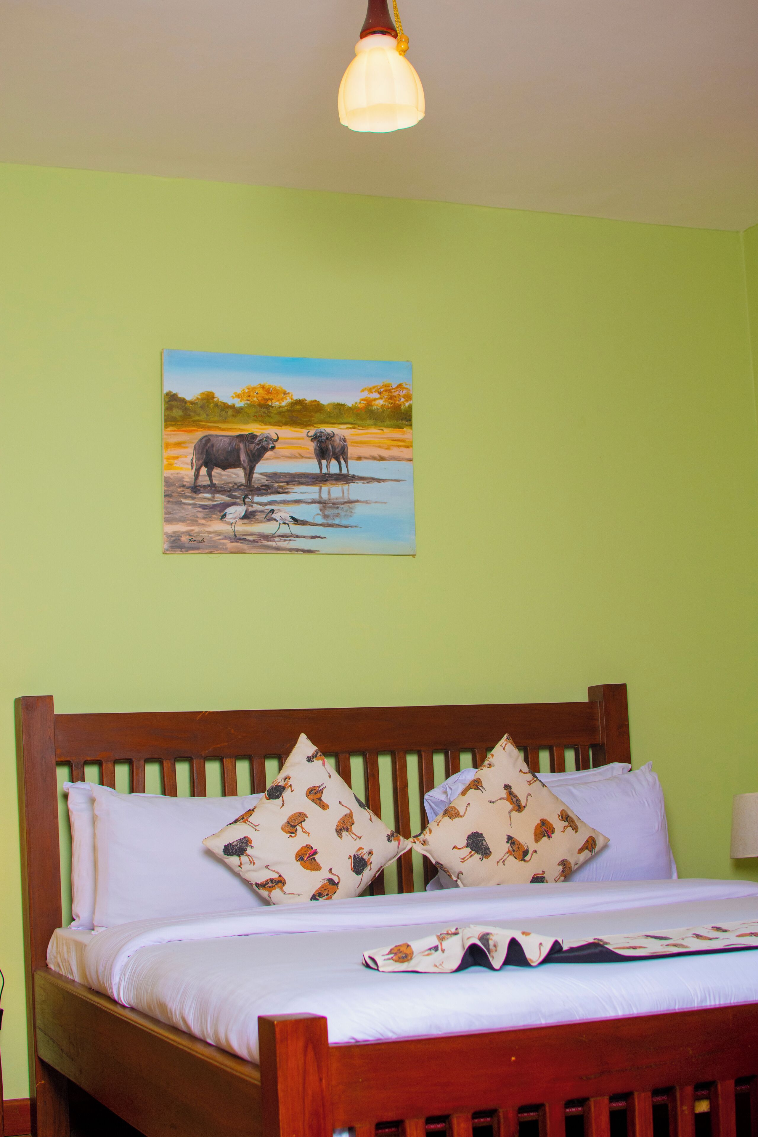 A bed with a wooden headboard, two patterned pillows, and a painting of wildlife on the wall.