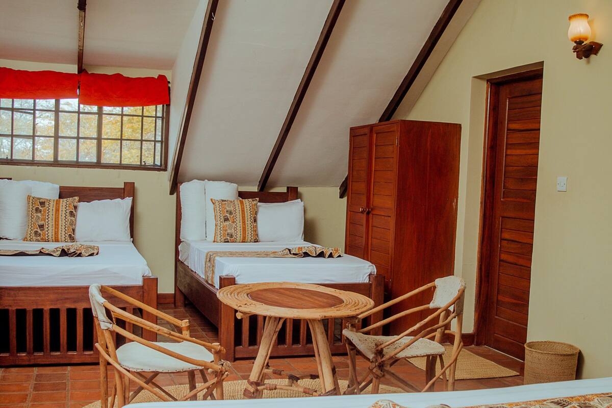 Ein Zimmer mit zwei Betten, einem Holztisch und Korbstühlen.