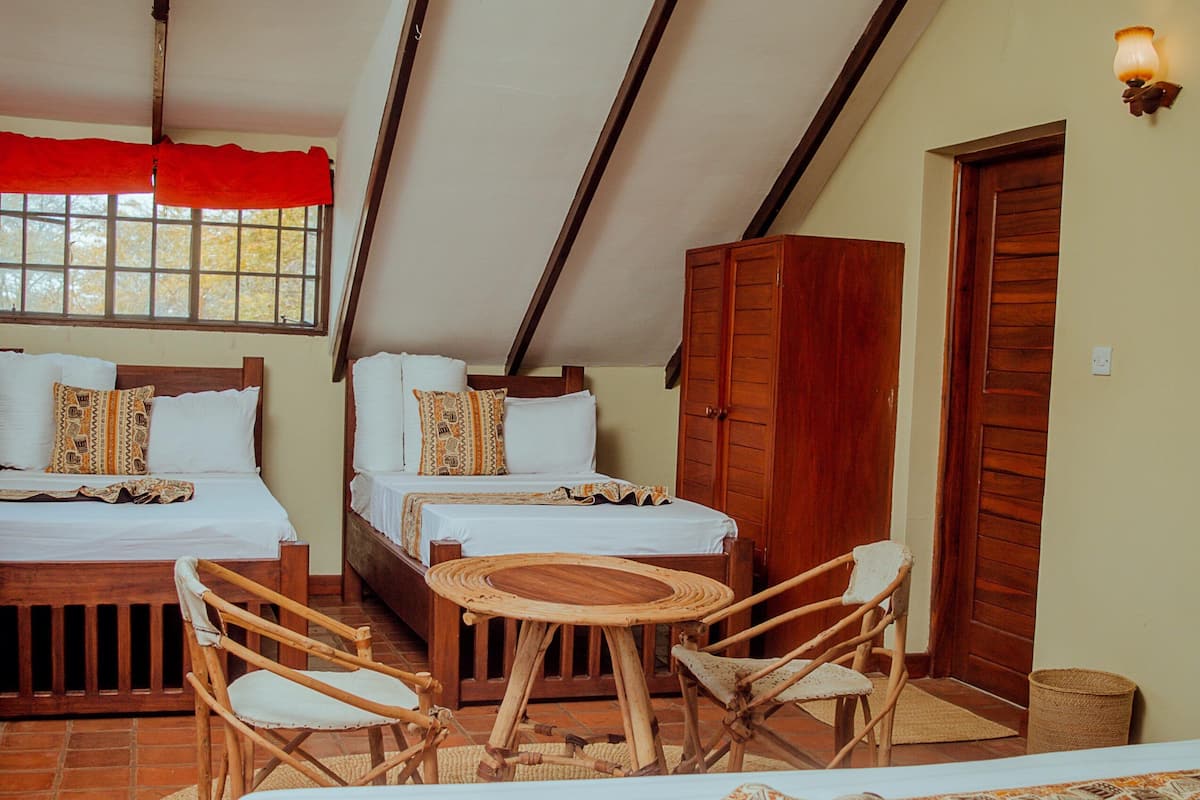 A room with two beds, a wooden table, and wicker chairs.