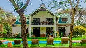 A two-story house with a swimming pool, surrounded by grass and trees. - Amani Farmhouse (Arusha)