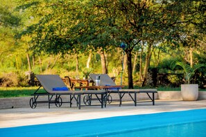 A poolside area with lounge chairs and a table, surrounded by greenery. - Amani Farmhouse (Arusha)
