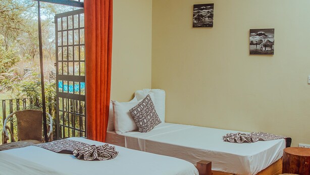 A room with two beds, a wooden table with a tray, a hanging light fixture, and a view of the outdoors. - Amani Farmhouse (Arusha)