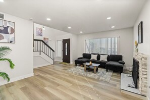 A modern living room with a staircase, a sofa set, and a fireplace. - Optional Heated Pool/Spa • BBQ Grill • Pacman Arcade • Foosball • King Bed (Las Vegas)