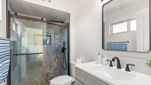 Ein modernes Badezimmer mit einer gläsernen Duschkabine, einer wei ßen Toilette, einem weißen Waschbecken mit schwarzen Armaturen und einem großen Spiegel über dem Waschbecken.
