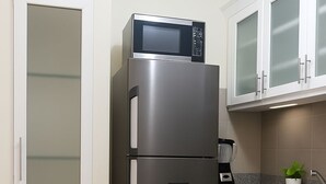 Un réfrigérateur en acier inoxydable, avec un four à micro-ondes sur le dessus, une machine à café et une plante en pot sur le comptoir de la cuisine.