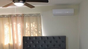 Une chambre à coucher avec une tête de lit capitonnée, un lit avec une literie à motifs, une table de chevet, un ventilateur de plafond et un appareil de climatisation.