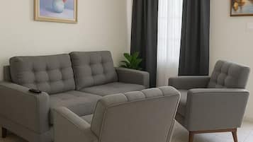 A living room with a grey sectional sofa, two armchairs, a ceiling fan, and a painting of flowers.