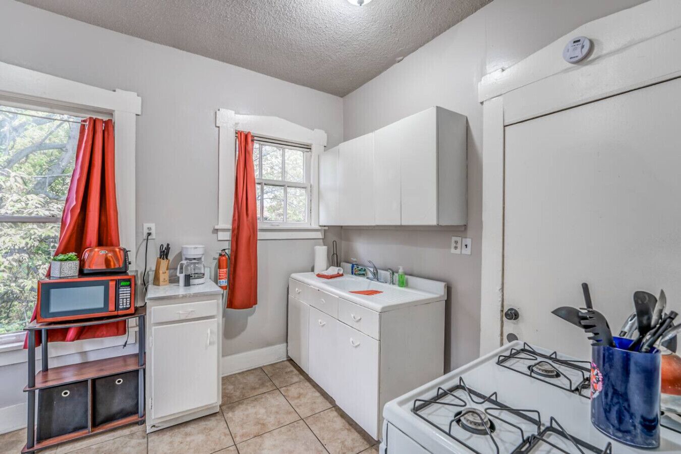 A compact kitchen with a gas stove, white cabinets, a microwave, and a small sink.