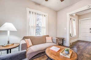 Un salon chaleureux avec un canapé, une lampe, une petite table sur laquelle se trouve un livre et une plante, et une porte visible au fond.