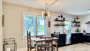 A modern kitchen with a dining area, featuring a central island, dark cabinetry, and a unique chandelier.