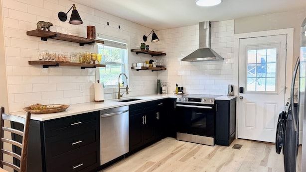 A modern kitchen with black cabinets, white subway tiles, wooden flooring, and built-in appliances.