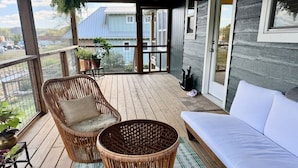 A wooden deck with wicker furniture, a white sofa, and a potted plant.